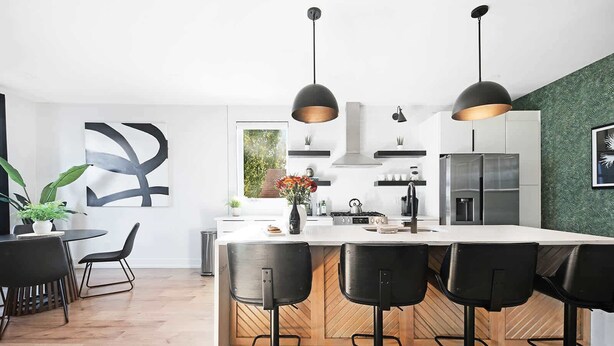 Una cocina moderna con una isla central, taburetes de bar, iluminación colgante y vistas al exterior.