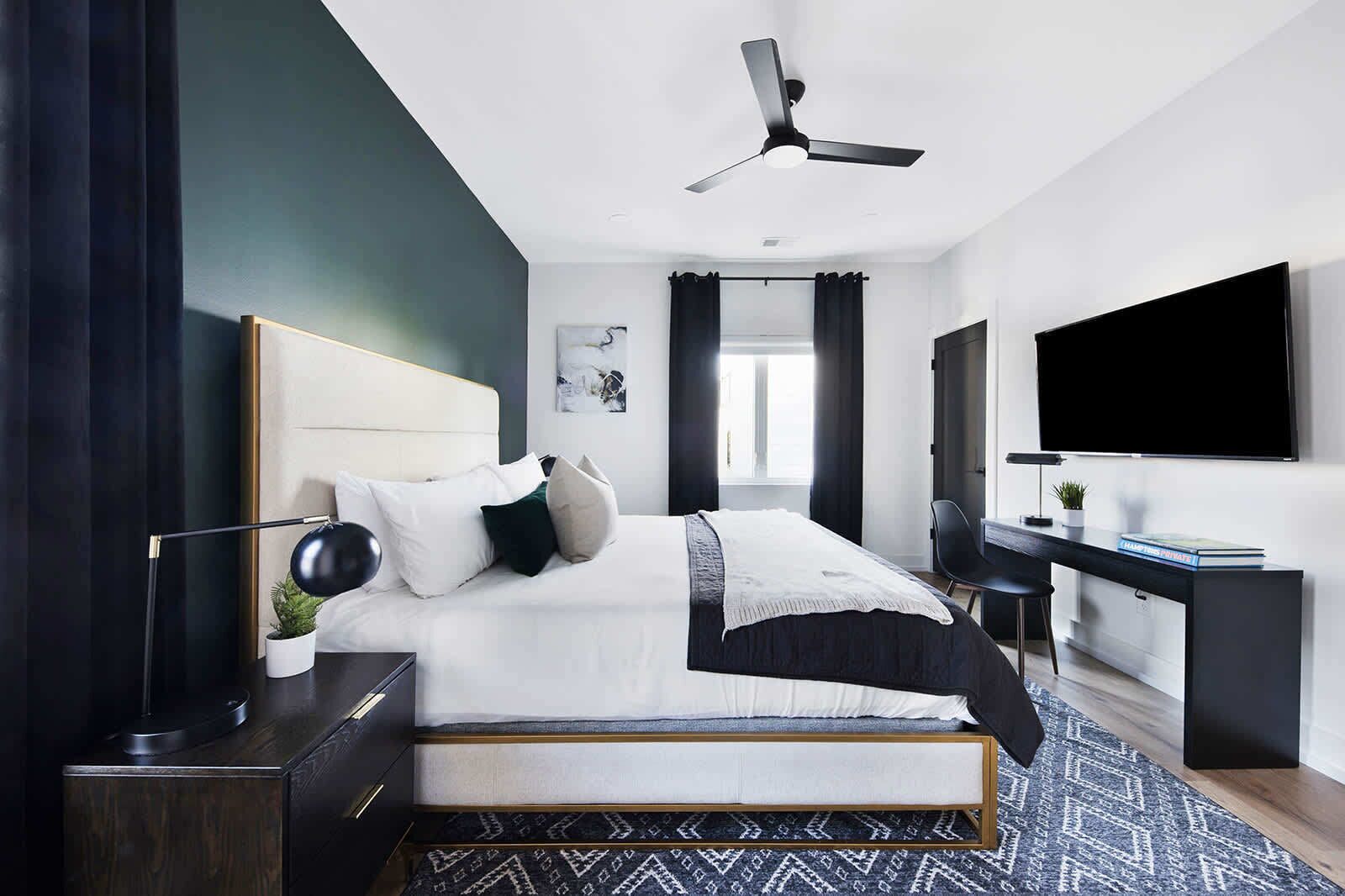 A modern bedroom with a bed, bedside table, desk, and a large TV.