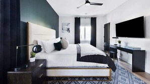 Un dormitorio moderno con cama, mesita de noche, escritorio y un televisor grande.