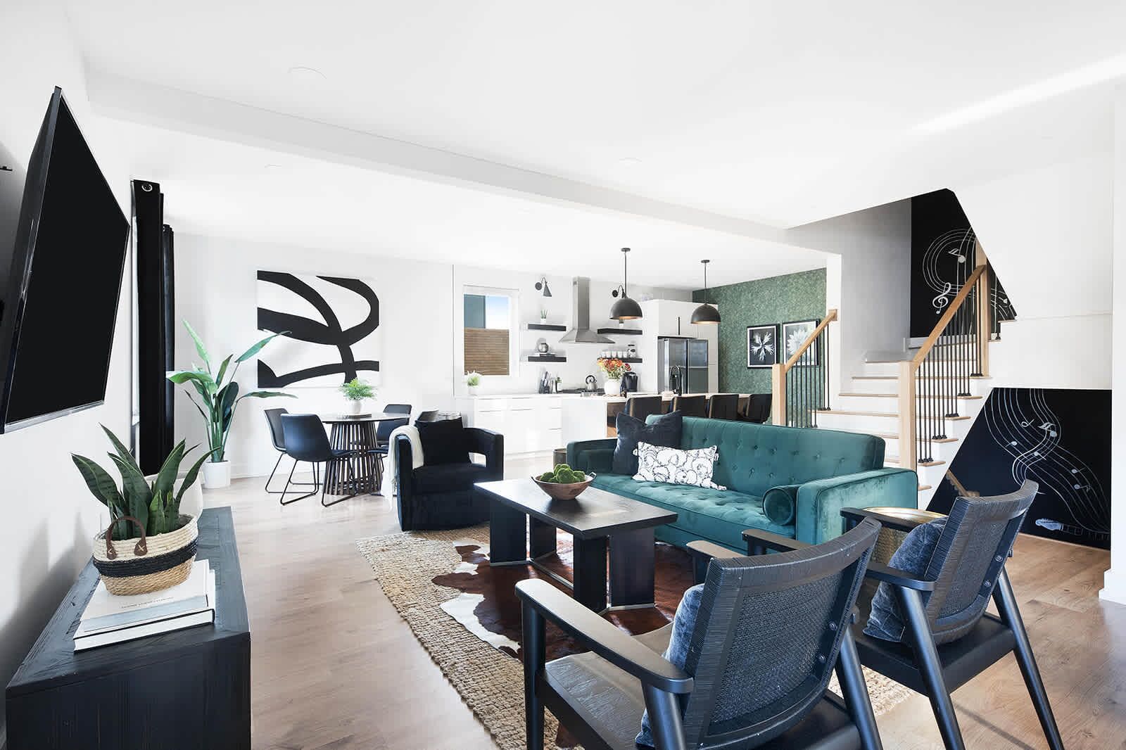 A modern living room with a teal sofa, black chairs, and a dining area with a table and chairs.