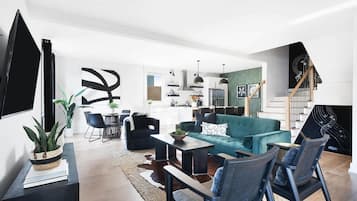 A modern living room with a teal sofa, black chairs, and a dining area with a table and chairs.