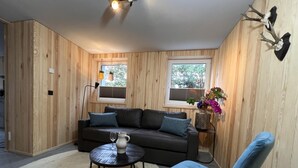 A cozy room with a dark brown sofa, a blue chair, a small round table with a glass pitcher, and two windows with blinds. - Bergquell Willingen App. 2 (Willingen)