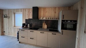 A modern kitchen with wooden panel walls, a black induction cooktop, a built-in oven, and a refrigerator. - Bergquell Willingen App. 2 (Willingen)