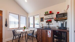 Una cocina con una mesa de comedor redonda, sillas negras, armarios de madera, un refrigerador negro y un microondas en un estante.