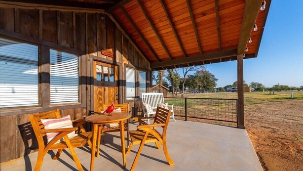 Un porche techado con muebles de madera, un comedero para pájaros y vistas a un campo cercado.