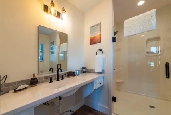A modern bathroom with a large mirror, two sinks, a shower enclosure, and a towel rack.