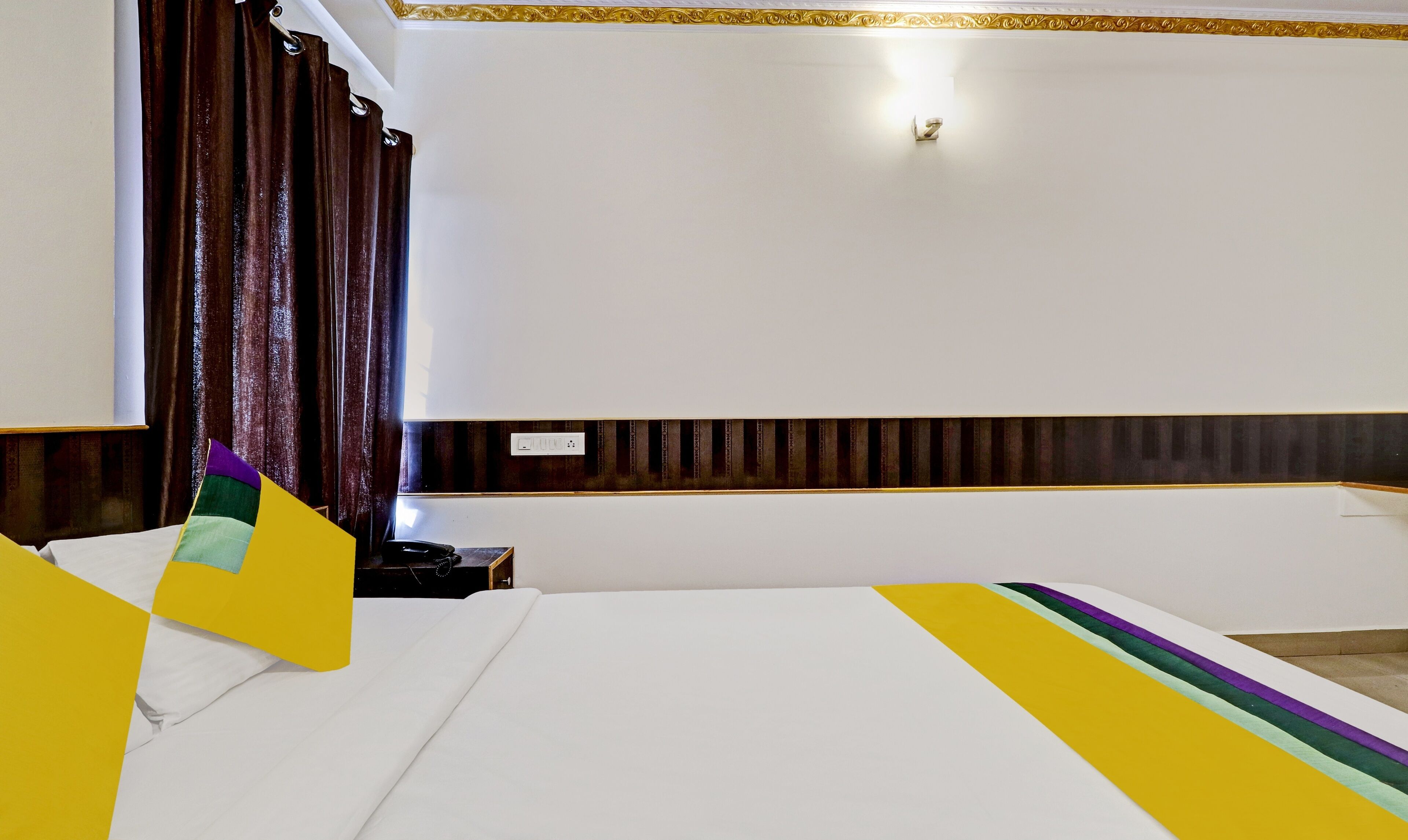 A hotel room with a large bed, a bedside table with a telephone, and a window with curtains.