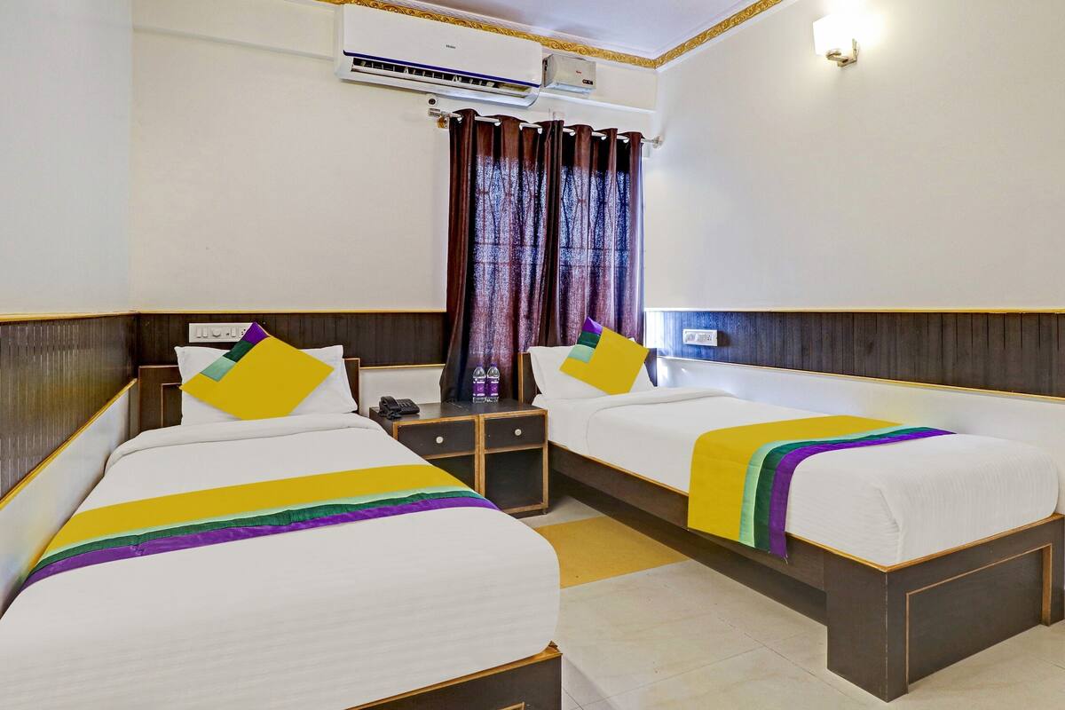 Een hotelkamer met twee bedden, een nachtkastje, een telefoon, een airconditioning en een gordijn.