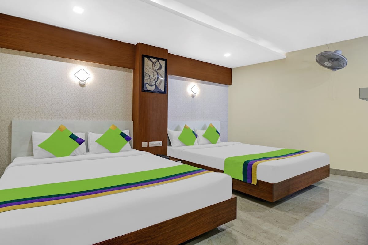 Habitación de hotel con dos camas, cada una con una manta verde y morada, cabeceros de madera y un ventilador de pared.