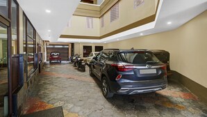 Un garage spacieux où sont garés plusieurs véhicules, dont un VUS bleu et une moto, et une voiture rouge est visible au fond.