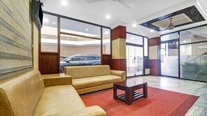 Un hall d’entrée avec un canapé beige, une petite table et un tapis rouge. Une porte vitrée donne sur l’extérieur, et on peut apercevoir une voiture à travers cette porte.