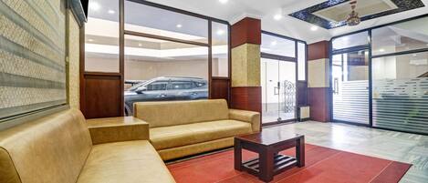 Un hall con un sofá color beige, una mesita y una alfombra roja. Se ve una puerta de vidrio que da al exterior, y un coche es visible a través de la puerta.
