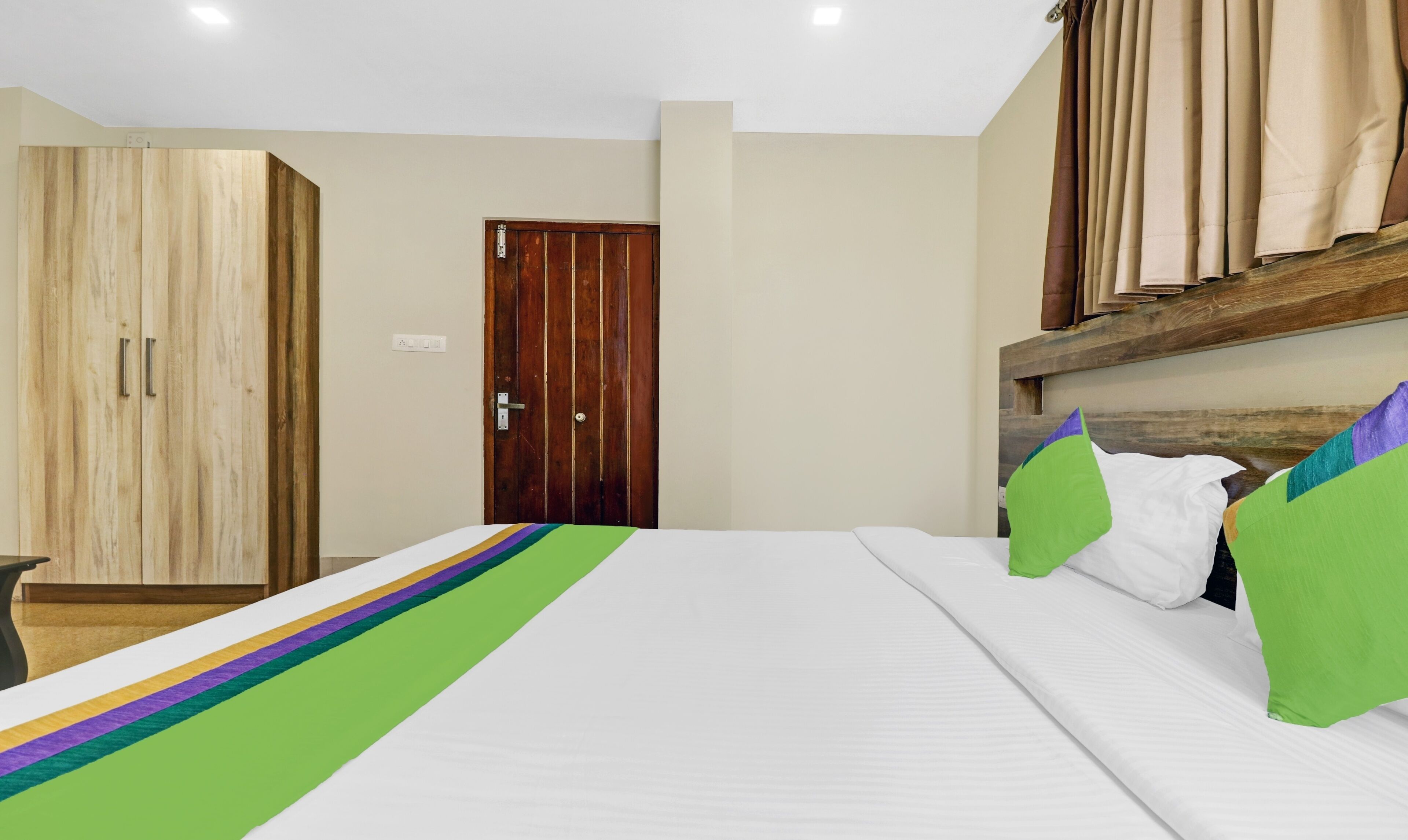 A bedroom with a bed, a wooden wardrobe, a door, and a headboard with curtains.
