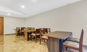 Uma área de refeições com mesa e cadeiras de madeira, piso de mármore e teto branco com iluminação embutida.