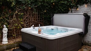 Ein Whirlpool mit einer Flasche und einem Glas, umgeben von einer Ziegelmauer und Grünpflanzen.