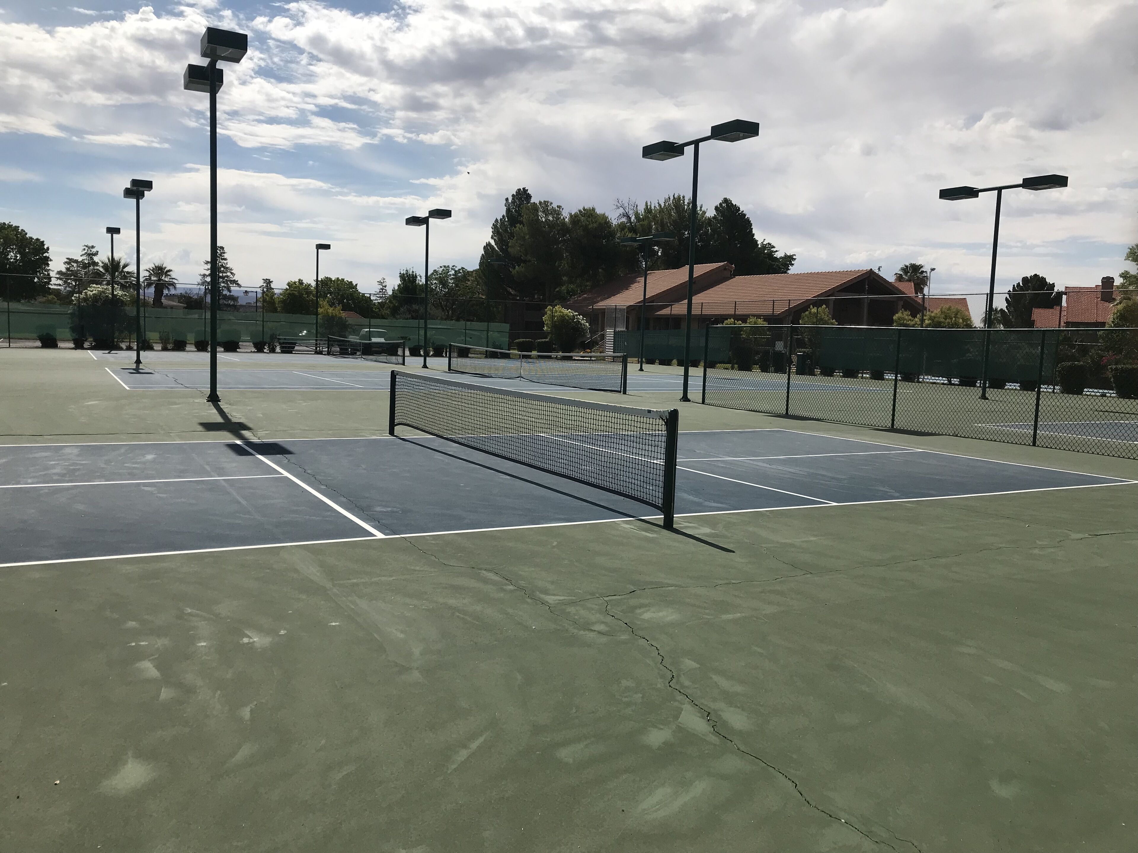 Een tennisbaan met meerdere velden, omringd door hekken en lantaarnpalen.