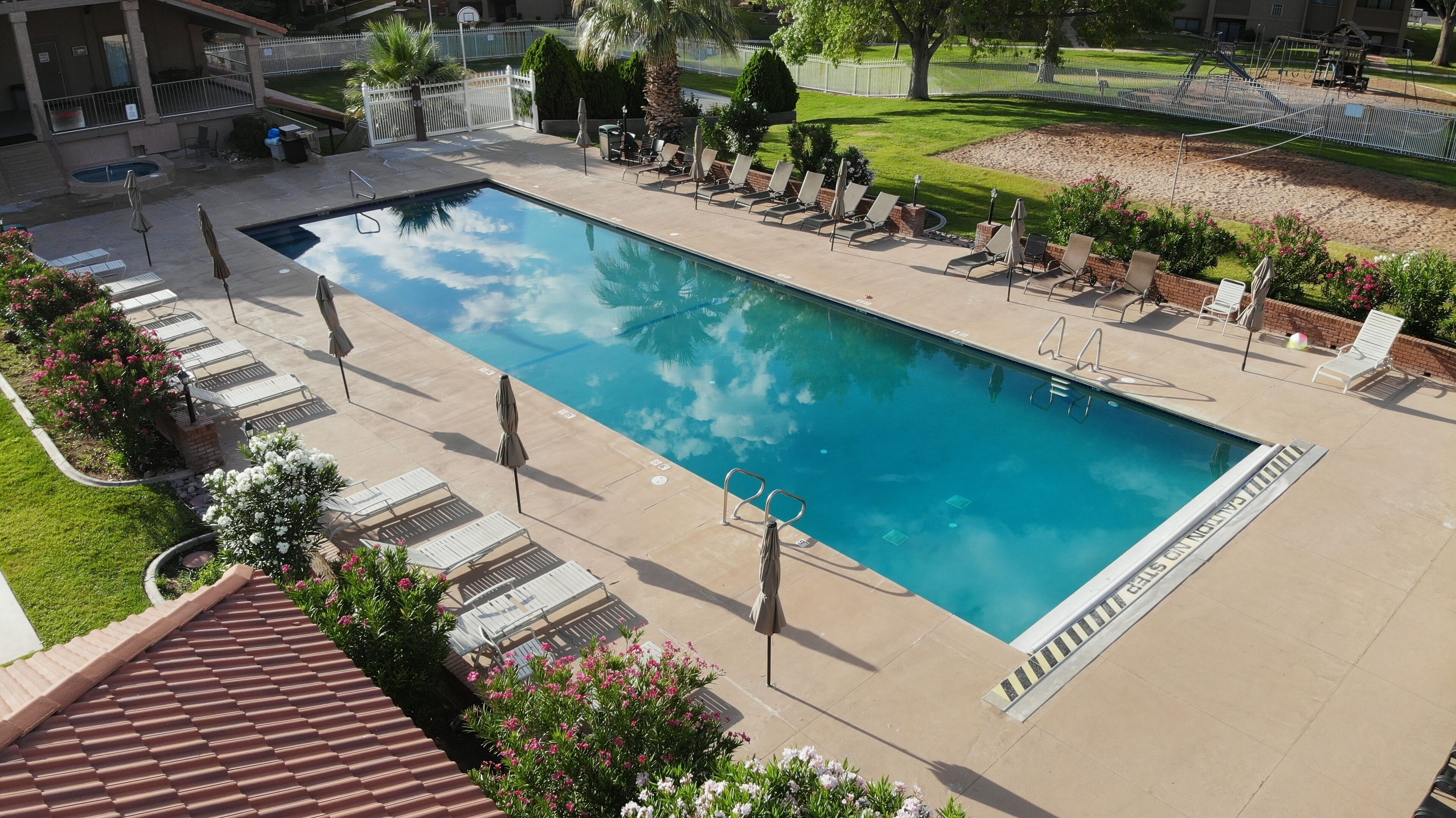 Ein rechteckiger Pool mit klarem, blauem Wasser, umgeben von Liegestühlen und Sonnenschirmen, mit einer Ziegelmauer und Grünpflanzen im Hintergrund.
