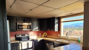 A kitchen with dark cabinets, stainless steel appliances, a window with a view of a desert landscape, and a tiled backsplash. - Beautiful 3 bedroom Sports Village Condo--sleeps 10. (St. George)