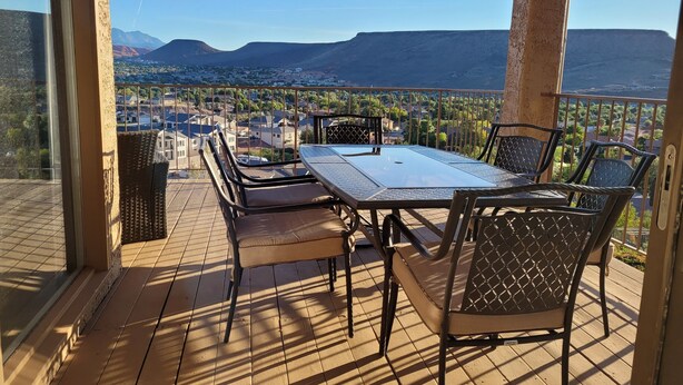 A balcony with a table and chairs, offering a view of a town and mountains. - Beautiful 3 bedroom Sports Village Condo--sleeps 10. (St. George)