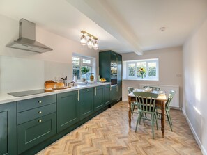 A kitchen with a herringbone floor, a dining area with a table and chairs, and a window with a view of greenery.