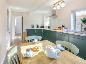 A bright kitchen with teal cabinets, a wooden dining table, and a white teapot.