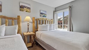 Camera d'albergo con due letti, una testiera in legno, un comodino con una lampada e una finestra che si affaccia su un paesaggio montano.