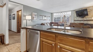 Una cocina moderna con una isla central, pileta de acero inoxidable, armarios de madera y lavavajillas integrado.