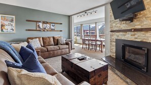 Una sala de estar con sofá, mesa de centro, chimenea y televisor montado en la pared.