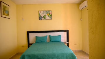 Un lit avec une couvre-lit de couleur turquoise et deux oreillers, un tableau accroché au mur et un appareil de climatisation.