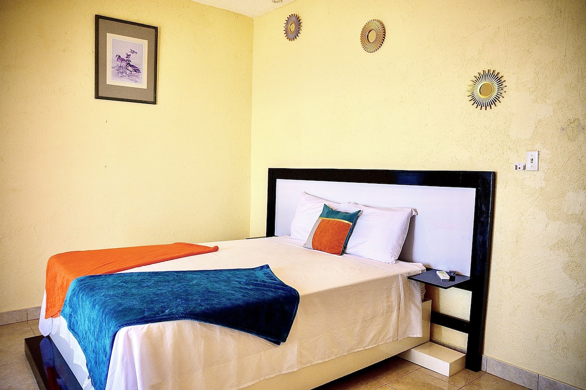 A neatly made bed with a blue and orange blanket, a small bedside table, and a wall-mounted decorative item.