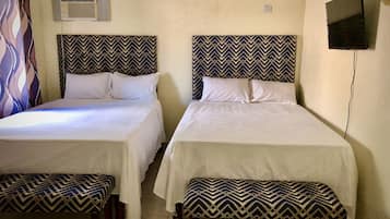 Dos camas individuales con cabeceras y pies de cama iguales, un televisor de pantalla plana montado en la pared y un equipo de aire acondicionado sobre las camas.