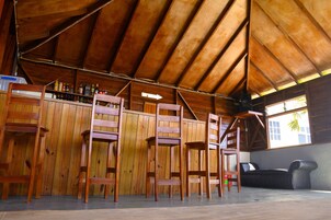 Un interior rústico de madera con techo alto, sillas de madera, zona de bar y un sofá negro.