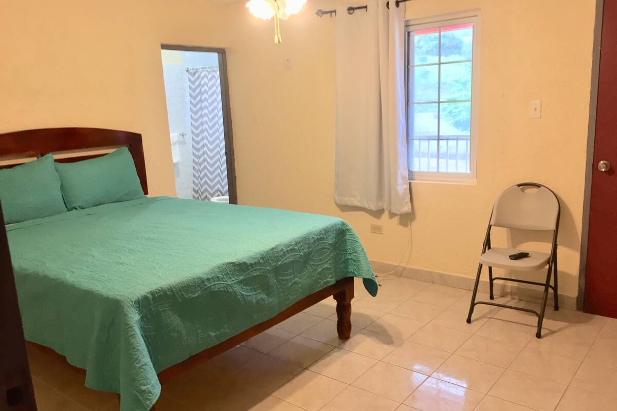 A bedroom with a bed, a chair, a window, and a door.