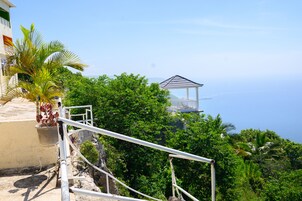 Vista costera con un pabellón, palmeras y un edificio con balcón con vista al mar.