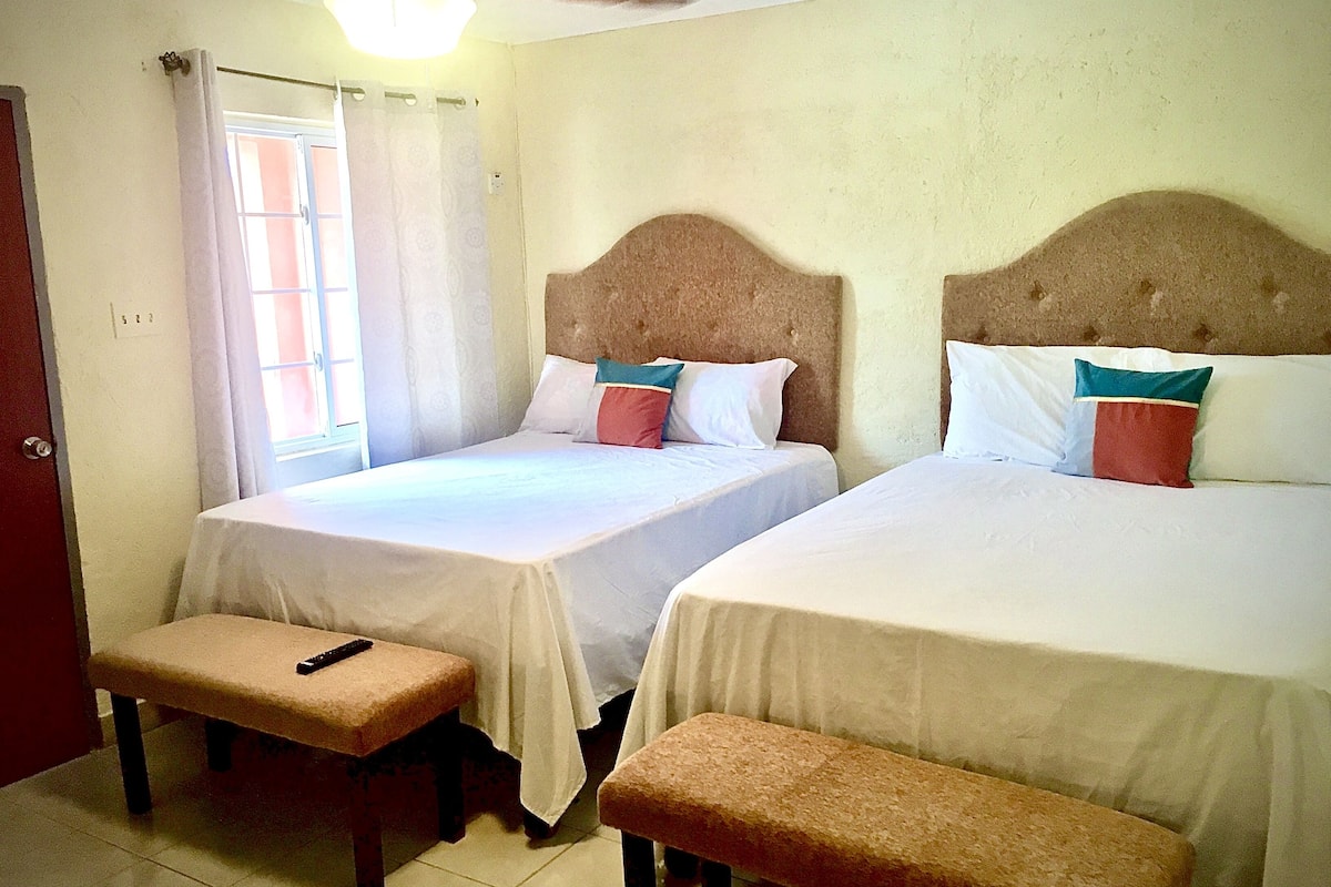 A hotel room with two beds, a bench, and a window with curtains.