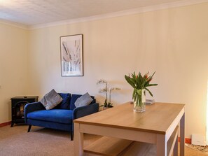 Una sala de estar con un sofá azul, una mesa de madera, un cuadro en la pared y un jarrón con flores sobre la mesa.