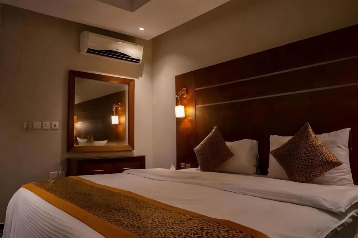 Habitación de hotel con una cama grande, cabecero con luces, un espejo y un equipo de aire acondicionado.