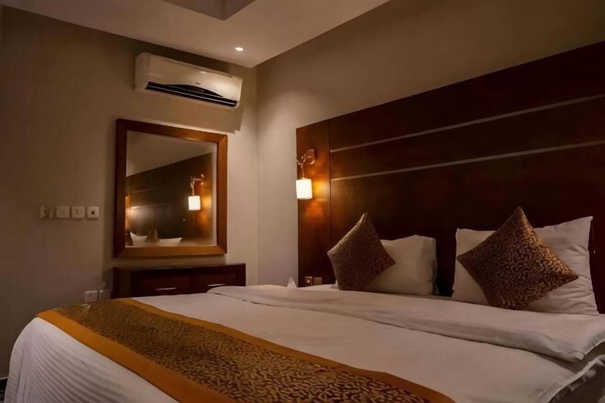 Quarto de hotel com uma cama grande, cabeceira com iluminação, espelho e aparelho de ar condicionado.