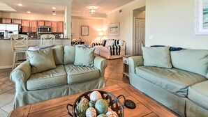 A living room with two light green sofas, a wooden coffee table with a basket of artichokes, and a kitchen in the background. - Screened Patio & Resort Perks: Bradenton Condo! (Bradenton)