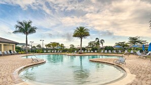 A swimming pool with a curved edge, surrounded by lounge chairs and palm trees. - Screened Patio & Resort Perks: Bradenton Condo! (Bradenton)