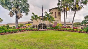 A building with a flagpole, surrounded by a well-maintained lawn and various plants. - Screened Patio & Resort Perks: Bradenton Condo! (Bradenton)