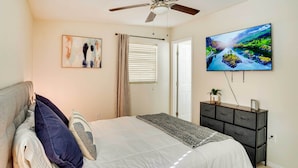Une chambre à coucher avec un lit, un ventilateur de plafond, un tableau, une télévision et une commode.