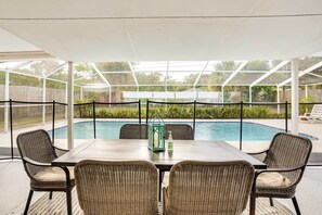 Eine überdachte Terrasse mit Pool, Korbstühlen und einem Tisch mit Laterne und Flasche.