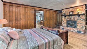 Un dormitorio con pared de paneles de madera, chimenea de ladrillo, cama con ropa de cama estampada y un banco.