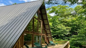Eine Holzterrasse mit Stühlen, einem Metalldach und bewaldeter Umgebung.