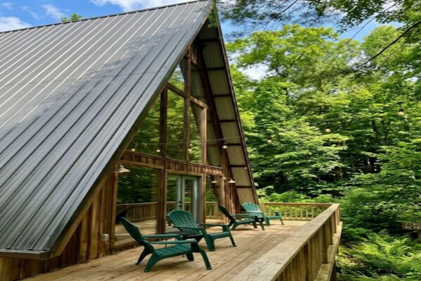 A wooden deck with chairs, a metal roof, and a forested backdrop.
