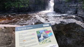 A waterfall with a sign titled "Force of Nature" describing geological features.