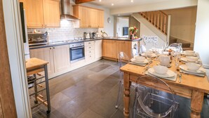 A modern kitchen with wooden cabinets, a built-in oven, and a dining area set for six. - Low Shipley Mill (Barnard Castle)