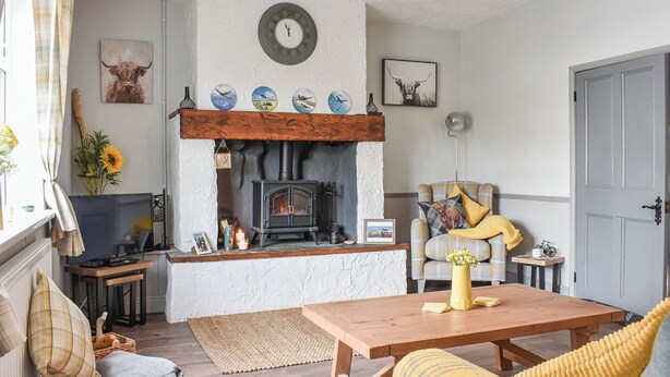 Una sala de estar acogedora con chimenea, una mesa de madera, un sillón a cuadros y un televisor.