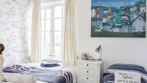 Un dormitorio con cama, mesita de noche, lámpara, cuadro y ventana con cortinas.